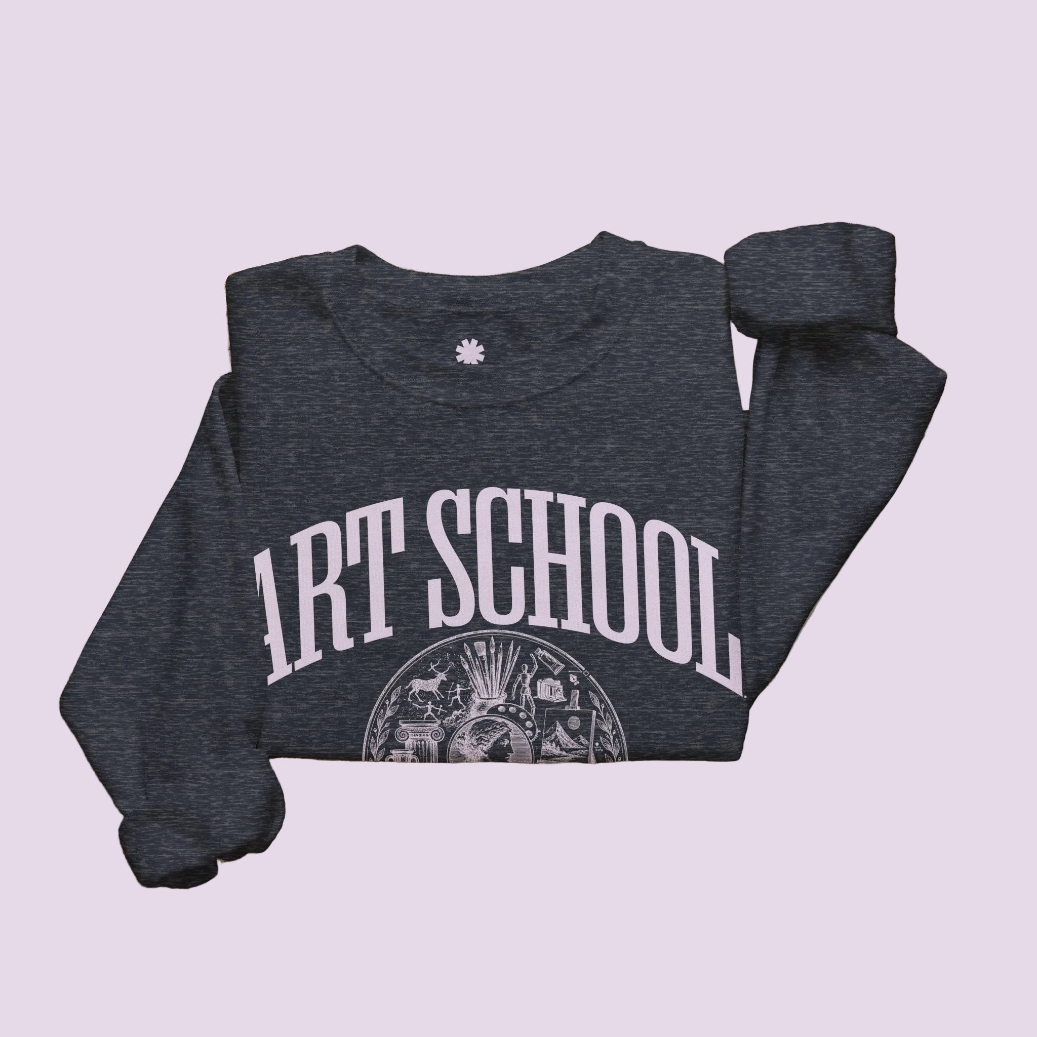 A folded heather navy sweatshirt with 'ART SCHOOL' printed in white across the front, styled on a light beige surface with a cream knit blanket, a woven basket, a tan tote bag, and a small amber candle.