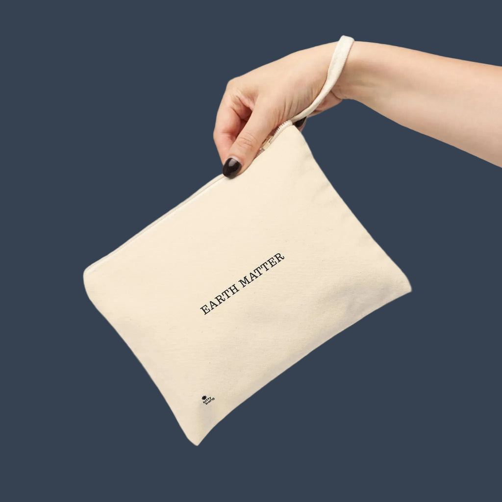 A hand holding a cream-colored canvas pouch with the text 'EARTH MATTER' printed in black on the front, set against a plain white background.